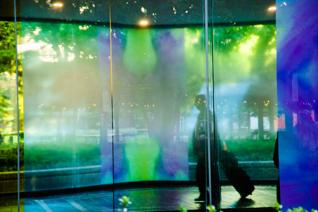 Figure moving through a luminous green glass architectural passage